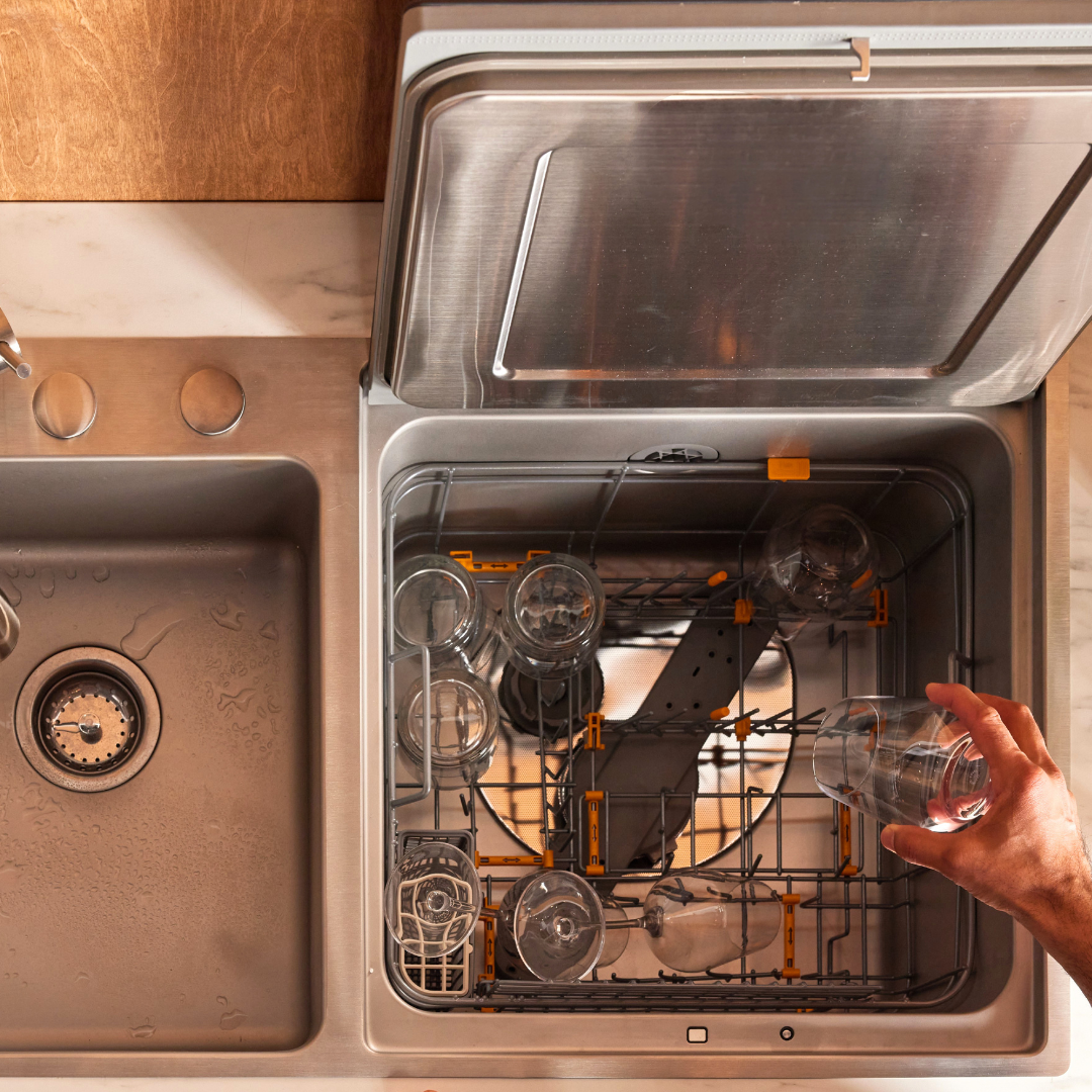 Hand loading a glass into a FOTILE in-sink dishwasher next to a kitchen sink