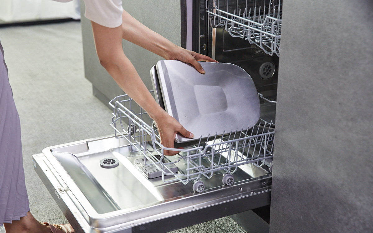 Person loading a tray into the lower rack of an open built-in dishwasher